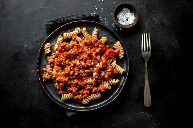 Pasta con salsa boloñesa servida en plato sobre fondo oscuro