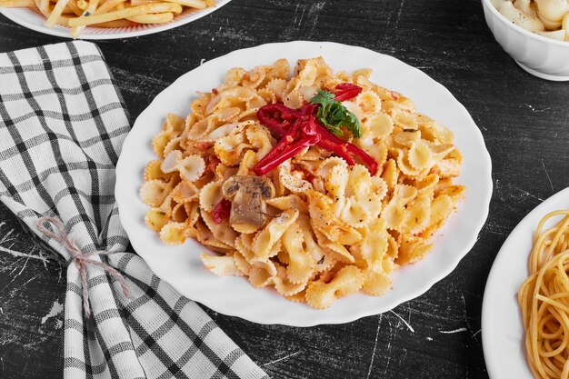 Pasta en salsa de tomate en un plato blanco sobre fondo negro.