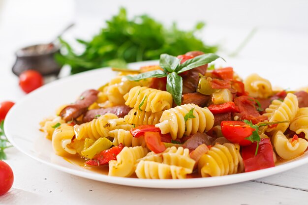 Pasta con salsa de tomate con salchicha, tomate, albahaca verde decorada en plato blanco sobre una mesa de madera.