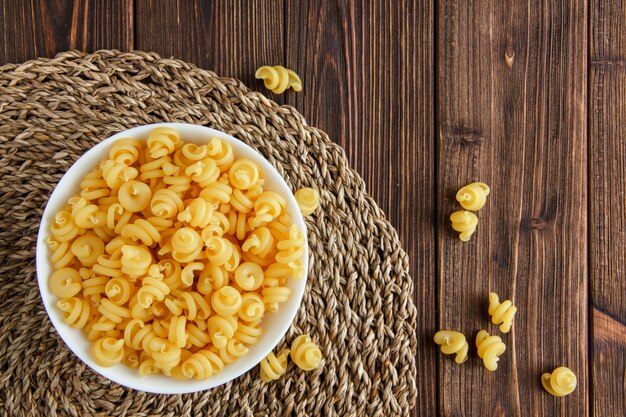 Pasta seca en un recipiente sobre fondo de mantel de madera y mimbre. aplanada