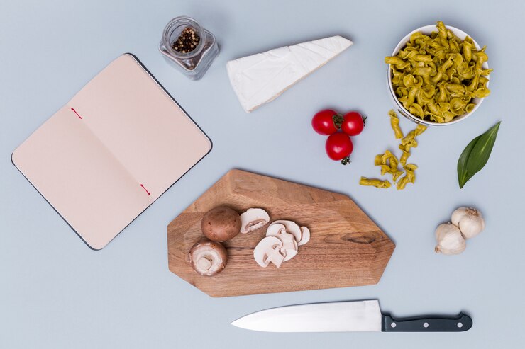 Foto gratuito pasta y su ingrediente con diario abierto en blanco sobre fondo liso