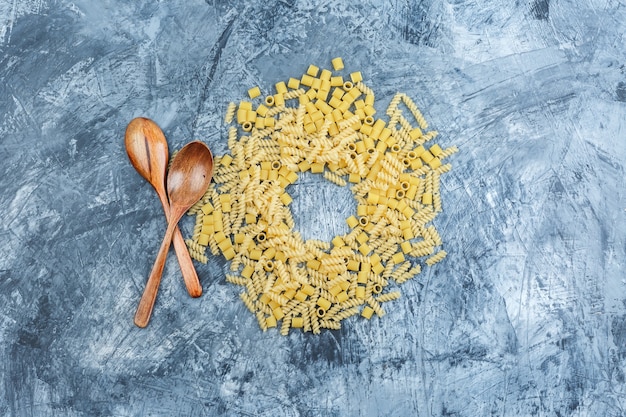 Pasta surtida laicos plana con cucharas de madera sobre fondo de yeso sucio. horizontal