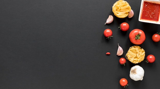 Pasta de tagliatelle cruda con diente de ajo; tomate; y salsa sobre fondo negro