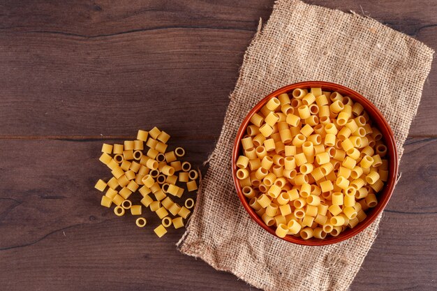 Pasta en un tazón marrón sobre tela de saco sobre superficie de madera