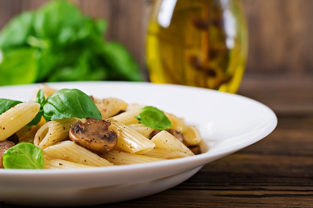 Pasta vegetariana pasta penne con setas en un tazón blanco sobre mesa de madera. Comida vegana.