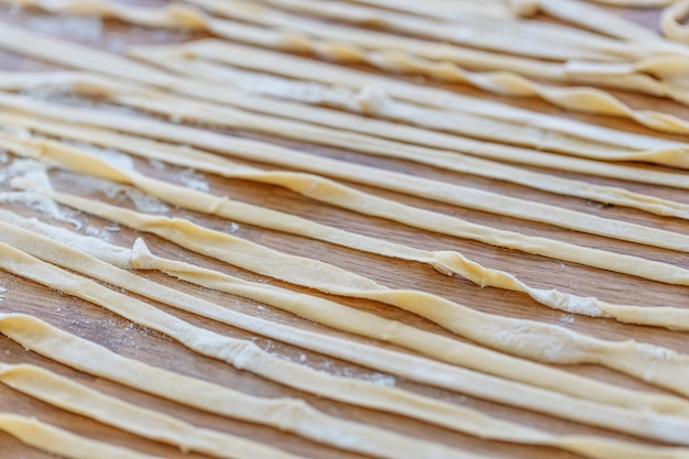 Pastas caseras frescas con harina sobre tabla de madera en la mesa.