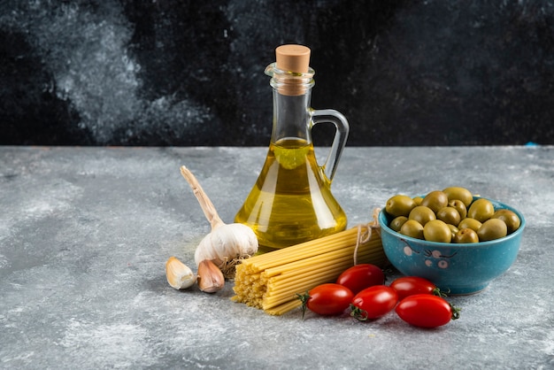 Pastas sin cocer, aceite y verduras frescas en la mesa de mármol.