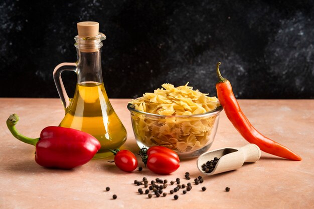 Pastas sin cocer, verduras y botella de aceite en la mesa naranja.