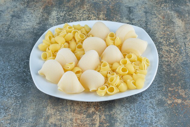 Pastas cocidas y crudas en el bol, sobre la superficie de mármol.