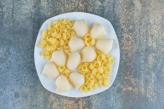 Pastas cocidas y crudas en el bol, sobre la superficie de mármol.