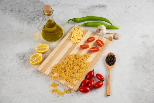 Pastas crudas, aceite y verduras frescas sobre mármol.