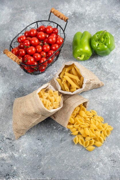 Pastas crudas en una bolsa rústica con tomates cherry y pimientos sobre mesa de mármol.