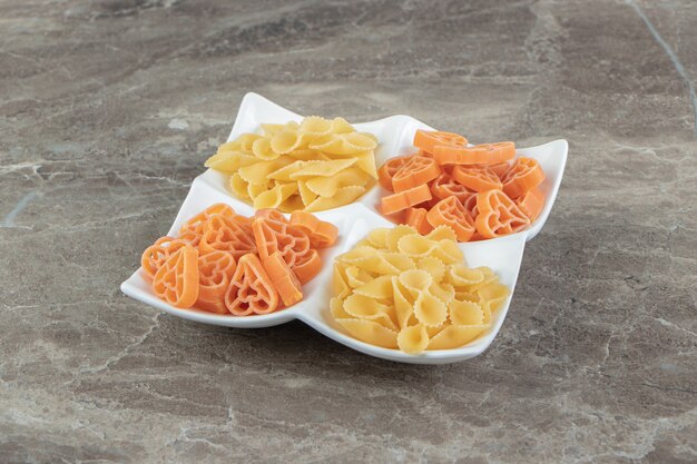 Pastas crudas en forma de corazón y de arco en un plato blanco.