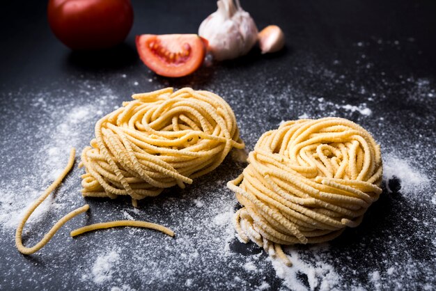 Pastas crudas hechas en casa anidan en harina con ajo y tomate en el fondo