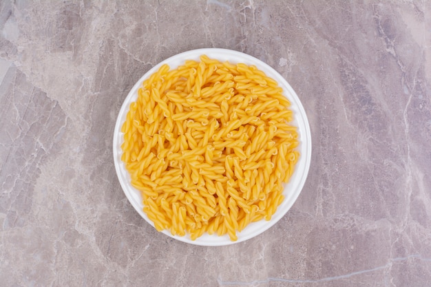 Pastas crudas en una taza de cerámica blanca sobre el mármol.