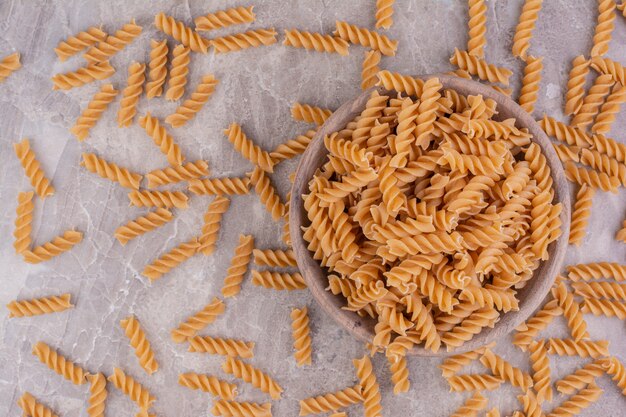 Pastas crudas en una taza de madera rústica y sobre el mármol gris.