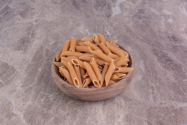 Pastas crudas en tazas de madera rústicas en espacio gris.