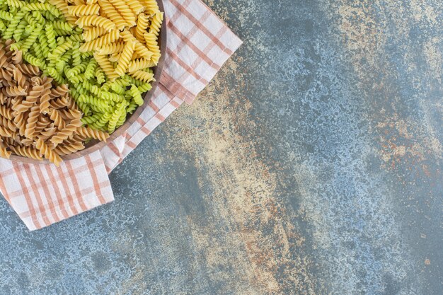 Pastas fusilli de colores en un recipiente sobre una toalla, sobre la superficie de mármol.