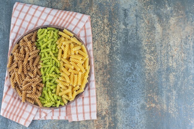 Pastas fusilli de colores en un recipiente sobre una toalla, sobre la superficie de mármol.