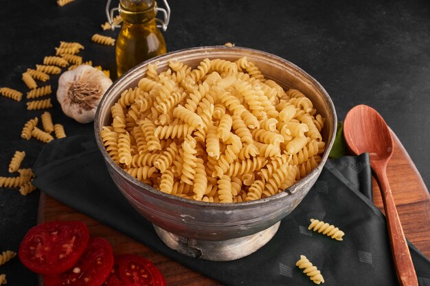 Pastas en taza metálica y sobre la mesa negra.