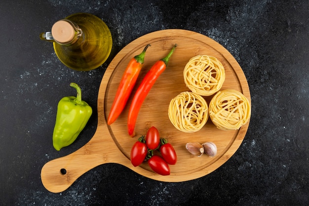 Pastas y verduras crudas sobre tabla de madera con aceite.