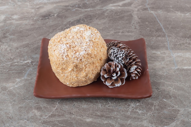 Pastel de ardilla y conos de pinos en un plato marrón sobre superficie de mármol