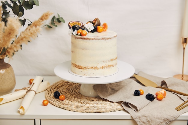 Pastel blanco con bayas y maracuyá junto a una planta detrás de un blanco