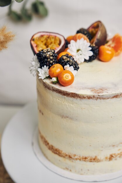 Pastel blanco con bayas y maracuyá junto a una planta detrás en blanco