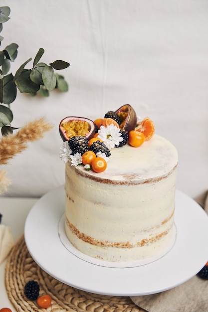 Pastel blanco con bayas y maracuyá junto a una planta detrás de un fondo blanco.