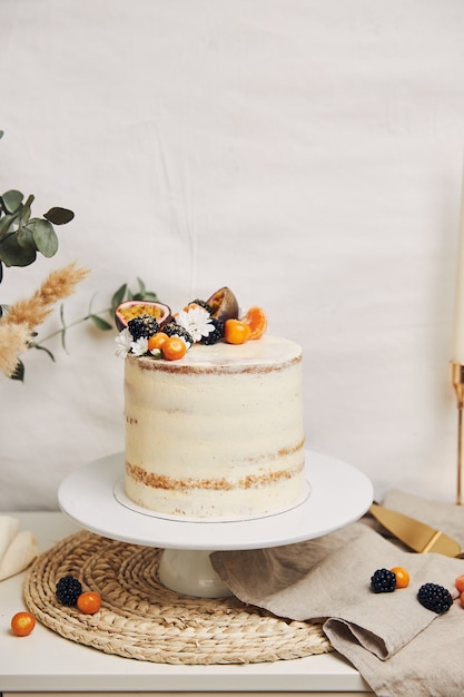 Pastel blanco con bayas y maracuyá junto a una planta detrás de un fondo blanco.