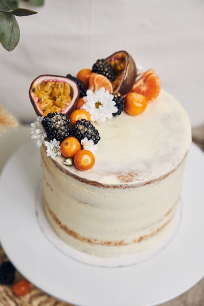 Pastel blanco con bayas y maracuyá junto a una planta detrás de un fondo blanco.