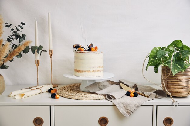 Pastel blanco con bayas y maracuyá junto a plantas y velas en blanco