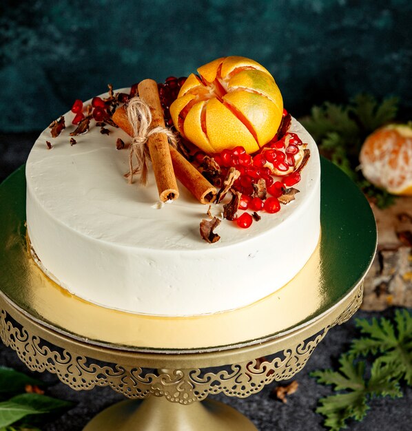 Pastel blanco cremoso decorado con palitos de canela y granadas de naranja