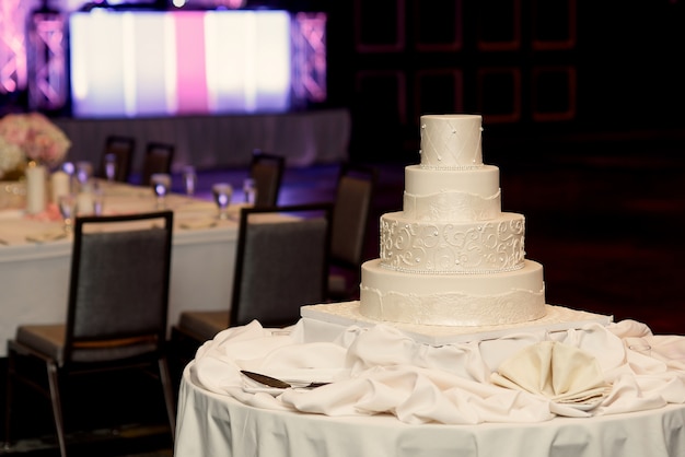 El pastel de bodas blanco cansado se coloca en la tela de seda en una cena