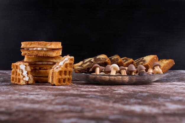 Pastel de cacao con gofres y galletas en una bandeja de vidrio sobre fondo negro