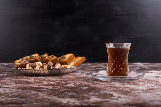 Pastel de cacao con gofres y galletas en bandeja de vidrio con un vaso de té