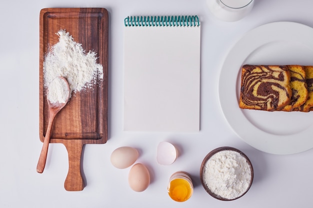 Pastel de cacao en rodajas y servido en un plato de cerámica blanca con ingredientes y un talonario de recibos alrededor.