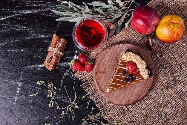 Pastel de chocolate decorado con crema y té de fresa, ciruela y canela sobre fondo oscuro.