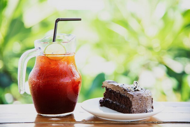 Pastel de chocolate en la mesa con té helado en el jardín verde - relájese con una bebida y una panadería en concepto de naturaleza