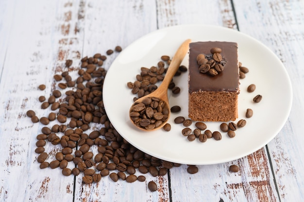 Pastel de chocolate en un plato blanco y granos de café en una cuchara de madera sobre una mesa de madera.