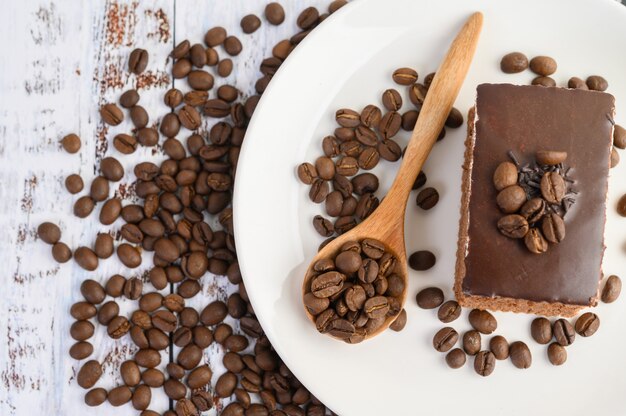 Pastel de chocolate en un plato blanco y granos de café en una cuchara de madera sobre una mesa de madera.