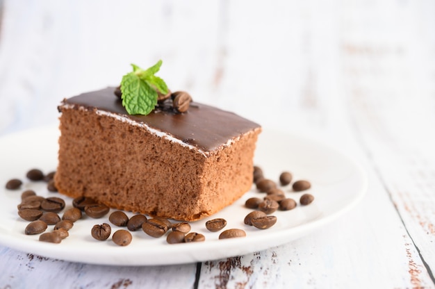 Pastel de chocolate en un plato blanco con granos de café sobre una mesa de madera