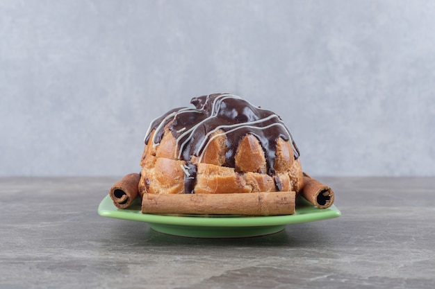 Pastel de chocolate y ramitas de canela en un plato pequeño sobre una superficie de mármol