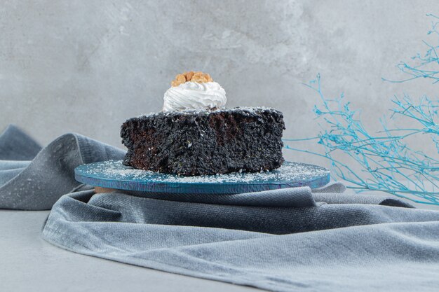 Pastel de chocolate recubierto con vainilla en polvo sobre una pequeña tabla sobre fondo de mármol.