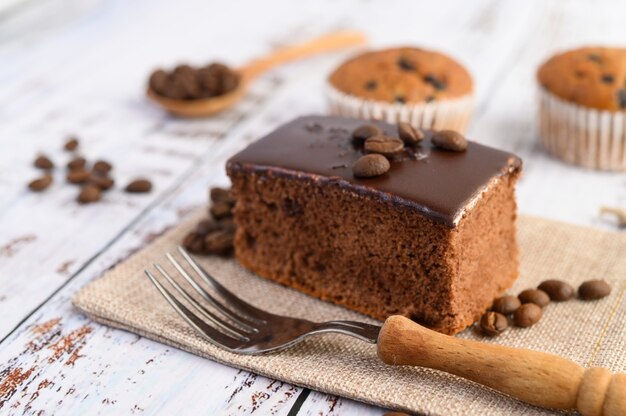 Pastel de chocolate en el saco y granos de café con un tenedor en una mesa de madera.