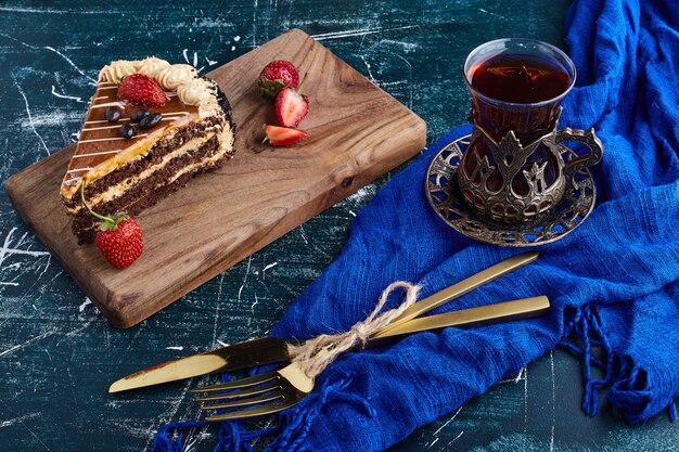 Pastel de chocolate servido con fresas sobre fondo azul con un vaso de té.