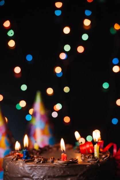 Pastel de chocolate con velas iluminadas y decorado con luces borrosas.