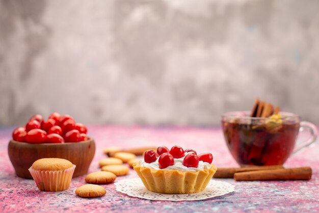 Pastel de crema de vista frontal con arándanos rojos frescos junto con galletas de canela y té en el brillante escritorio biscuit té dulce