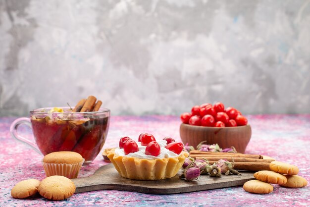 Pastel de crema de vista frontal con arándanos rojos frescos junto con galletas de canela y té en el dulce escritorio brillante