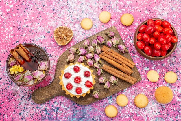 Pastel de crema de vista superior con arándanos rojos frescos junto con galletas de canela y té en la superficie brillante dulce de azúcar